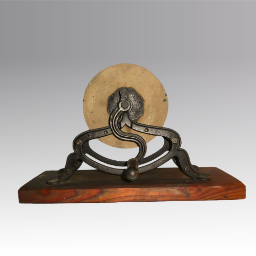 Round grindstone on a cast iron stand, turned by handle, mounted on a wooden base.