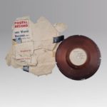Vinyl record next to a white envelop labelled "Postal Record" in red font.