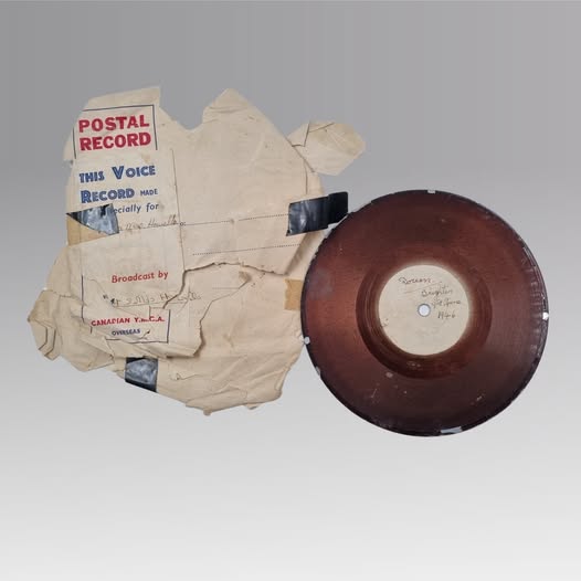 Vinyl record next to a white envelop labelled "Postal Record" in red font.